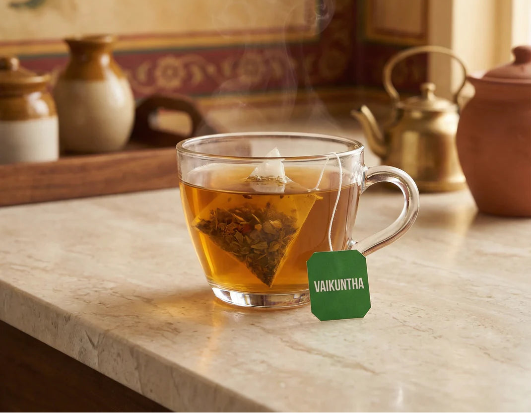 Clear glass mug with steaming tea and a 'VAIUKUNTHA' tag on a marble surface.